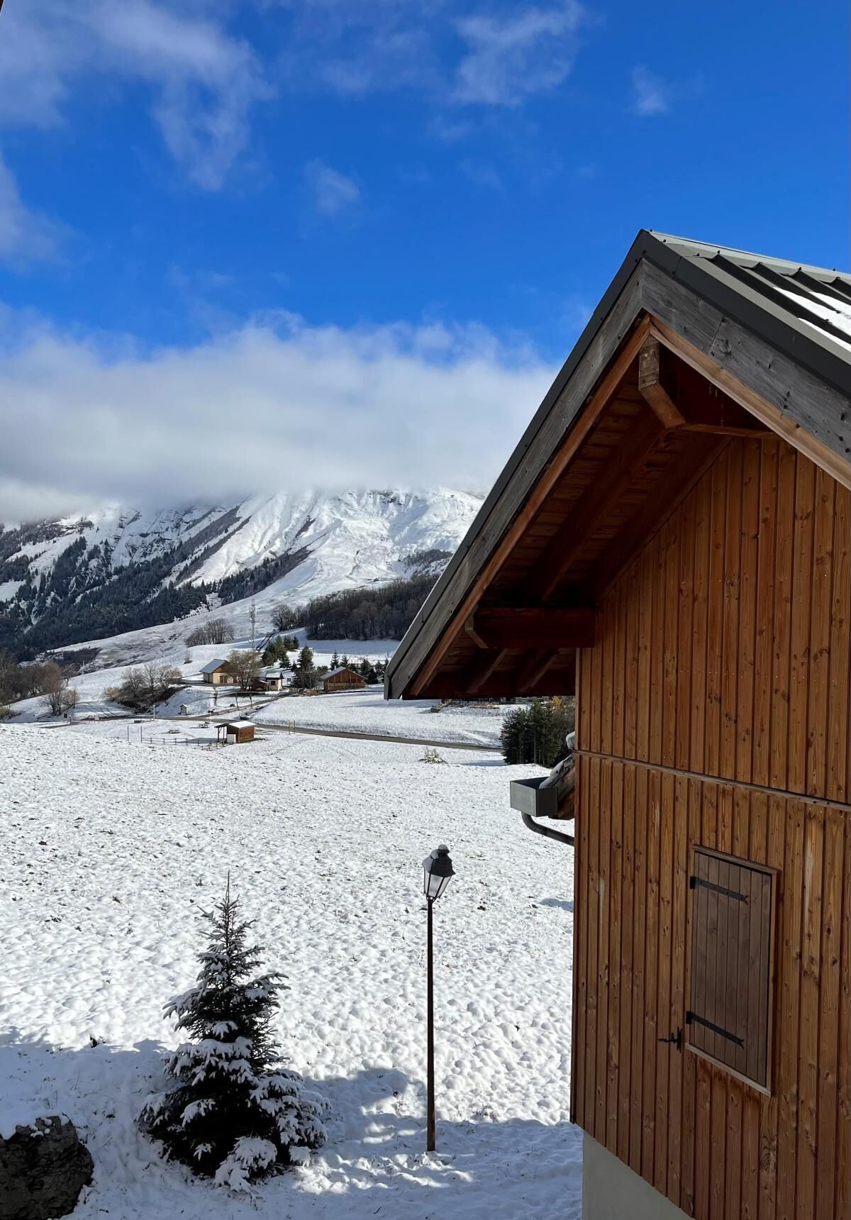 Een houten hut met een schuin dak, een met sneeuw bedekte grond en een bergachtig achtergrond.