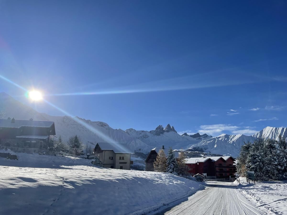 Un paysage enneigé avec des bâtiments, un ciel dégagé et des montagnes en arrière-plan.