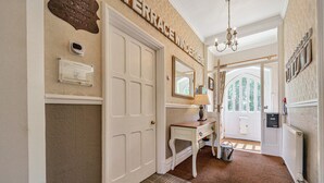 A hallway with a white door, a plaque, a mirror, a desk with a lamp, and a radiator. - Alice Howe - a big house with hot tub and cinema for groups to get together in the Lake District. (Windermere)