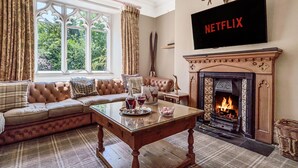 A cozy living room with a fireplace, a sofa, a coffee table with drinks, and a TV mounted above the fireplace. - Alice Howe - a big house with hot tub and cinema for groups to get together in the Lake District. (Windermere)