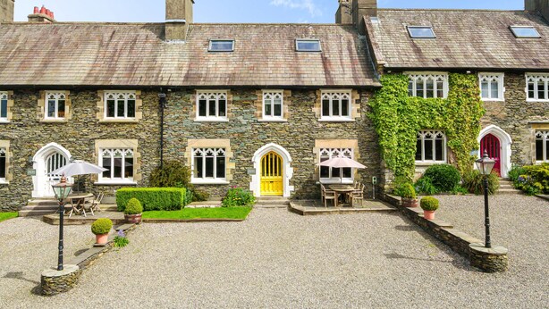 A stone building with multiple windows, a yellow door, and a gravel courtyard with outdoor seating. - Alice Howe - a big house with hot tub and cinema for groups to get together in the Lake District. (Windermere)