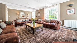 A spacious living room with a large brown leather sofa set, a wooden coffee table, and a plaid rug. - Orrest Head House, a majestic Lakeland property a moments walk from Windermere village. (Windermere)