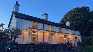 A two-story building with a stone wall entrance, multiple windows, and outdoor seating area with string lights. - Orrest Head House, a majestic Lakeland property a moments walk from Windermere village. (Windermere)