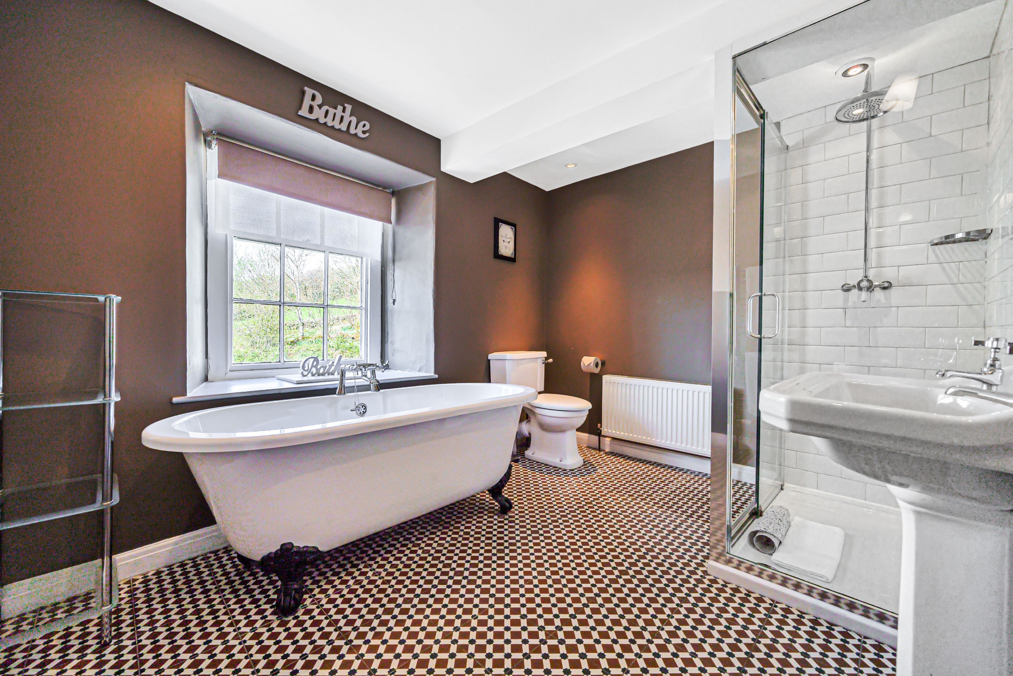 Une salle de bain comprenant une baignoire sur pieds, des toilettes, un espace douche et une fenêtre donnant sur un paysage verdoyant.