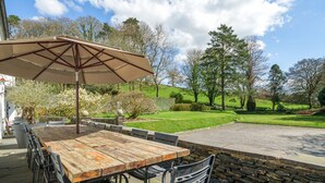 An outdoor patio with a wooden table and chairs, a stone wall, and a view of a green landscape. - Orrest Head House, a majestic Lakeland property a moments walk from Windermere village. (Windermere)