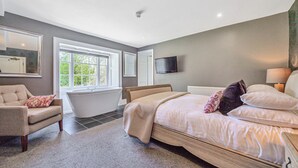 A bedroom with a large bed, a sitting area with a chair, a bathtub, and a television on the wall. - Orrest Head House, a majestic Lakeland property a moments walk from Windermere village. (Windermere)