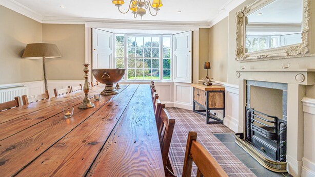 A dining room with a long wooden table, chairs, a chandelier, a fireplace, and a large mirror. - Orrest Head House, a majestic Lakeland property a moments walk from Windermere village. (Windermere)