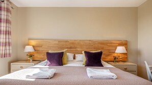 A neatly made bed with a headboard, two bedside tables with lamps, and a plaid curtain on the left. - Orrest Head Cottage,  located on the footpath to the famous Orrest Head walk. Perfect for dog walks. (Windermere)