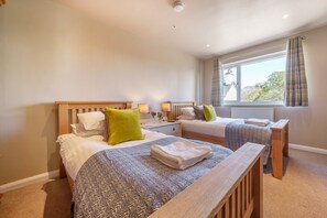 A hotel room with two beds, a window with curtains, a radiator, and a bedside table with a lamp. - Orrest Head Cottage,  located on the footpath to the famous Orrest Head walk. Perfect for dog walks. (Windermere)