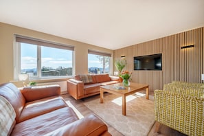 Relax in a spacious living room with a large window offering a view of the outdoors, a flat-screen TV, and a comfortable seating area.