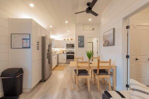 Uma cozinha moderna com armários brancos, uma área de refeições com mesa e cadeiras de madeira, e um ventilador de teto.