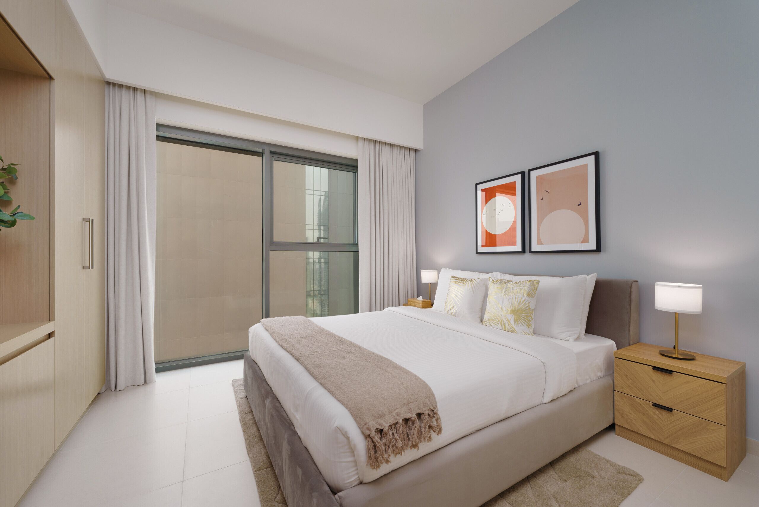 Un dormitorio moderno con una cama grande, una mesita de noche con lámpara y dos cuadros enmarcados en la pared.