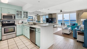 A modern kitchen with stainless steel appliances, a dining area with a white island, and a living room with a view of the ocean.