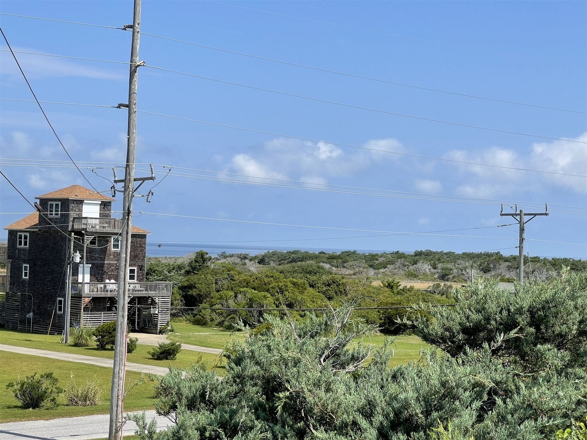 A two-story building with a balcony, surrounded by greenery and power lines.