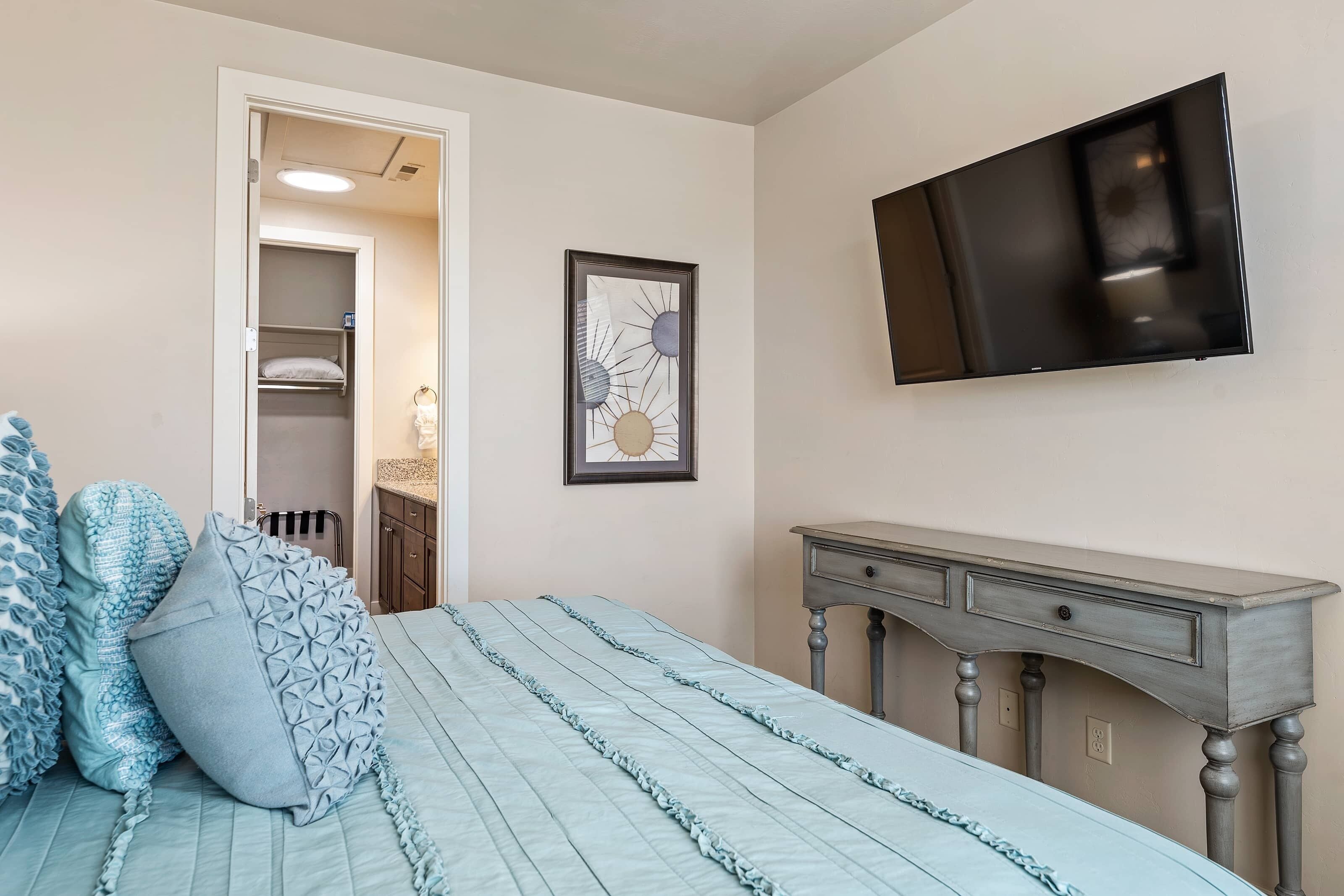 A bedroom with a bed, a dresser, a TV, and a framed picture on the wall.