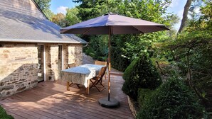 A stone house with a wooden deck, a table with chairs, and a large umbrella. - Maison de Campagne (Moulins)
