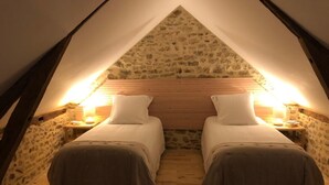 A cozy attic bedroom with two single beds, wooden headboard, stone walls, and a sloped ceiling. - Maison de Campagne (Moulins)