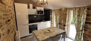 Una cucina compatta con frigorifero, forno, microonde e lavello. C'è un tavolo da pranzo con tovaglia fantasia e un lampadario sopra.