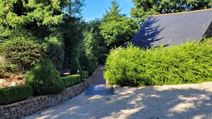 A gravel driveway leading to a stone-walled garden with neatly trimmed hedges and a variety of trees. - Maison de Campagne (Moulins)