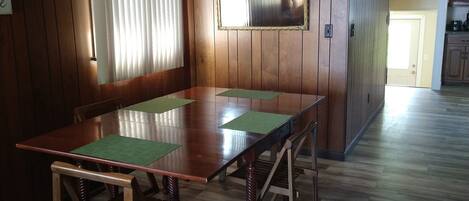 A dining area with a wooden table and chairs, a ceiling fan, and a window with blinds.