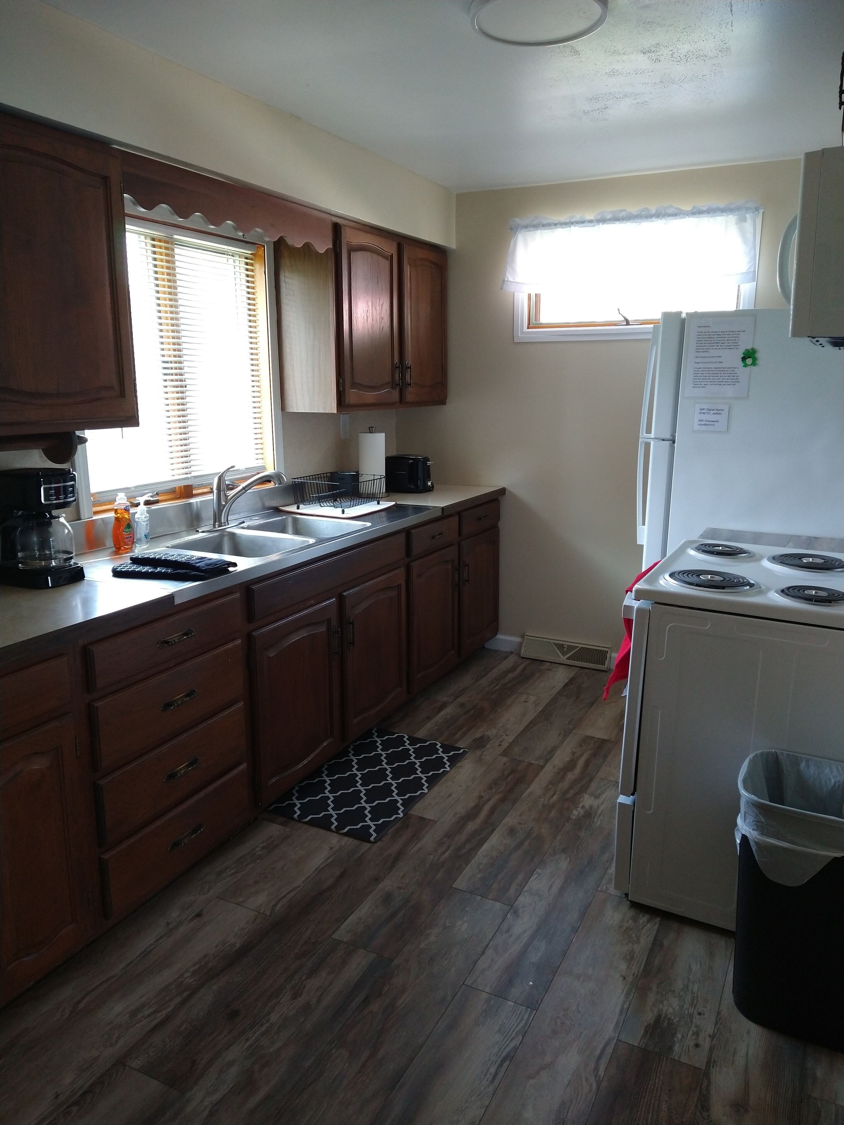 A kitchen with wooden cabinets, a stainless steel sink, a stove, and a window with blinds.