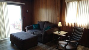 Ett mysigt rum med trägolv, en soffa, en gungstol och ett litet bord med en lampa.