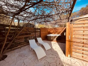 Relax in an outdoor space with a hot tub and lounge chairs under a shaded pergola.