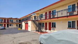 A multi-story motel with a red and beige facade, a covered parking area, and a staircase leading to the upper floors.