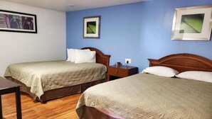 A hotel room with two beds, wooden flooring, and framed pictures on the walls.