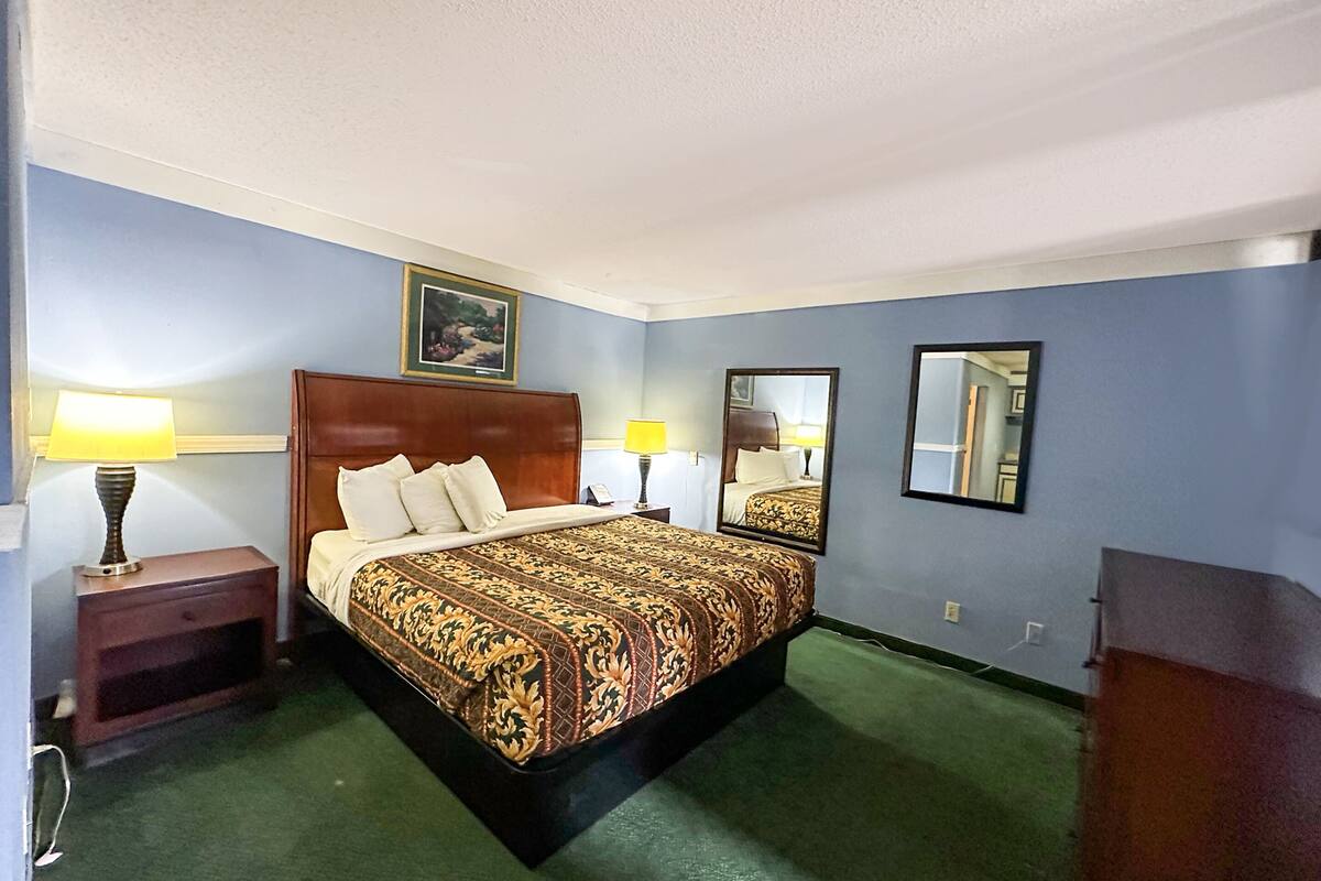 A hotel room with a large bed, two bedside lamps, a wooden headboard, a framed picture on the wall, and a mirror.