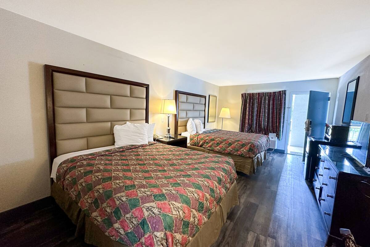 A hotel room with two beds, a TV, a dresser, and a door leading to a balcony.
