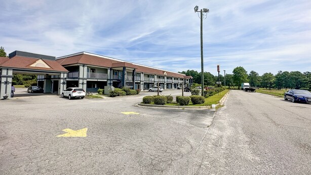 A hotel with a parking lot, a covered entrance, and a street with cars.