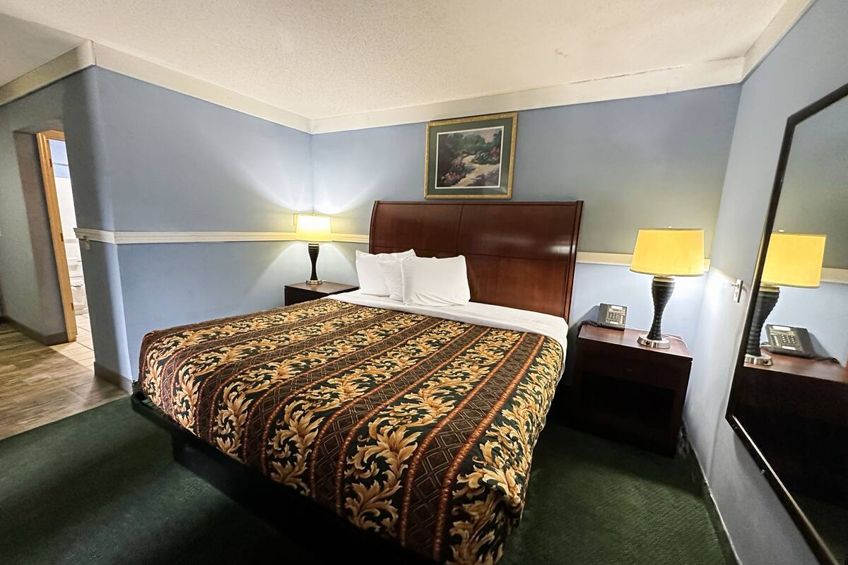 A hotel room with a large bed, a wooden headboard, two bedside tables with lamps, a painting on the wall, and a mirror.