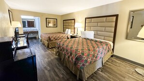 A hotel room with two beds, a desk, and a chair. There is a window with curtains, a painting on the wall, and a lamp on the desk.