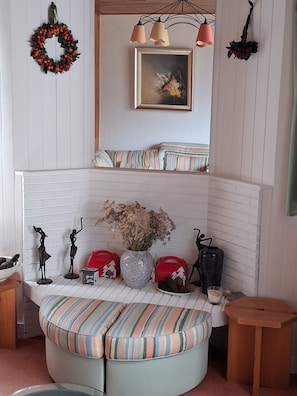 A corner seating area with a cushioned bench, a vase with dried flowers, and decorative items including a wreath and a framed painting. - VAL D'isere Centre Station (Val-d'Isère)