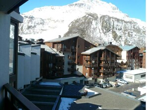 Un complejo turístico de montaña con varias construcciones de estilo chalet, un área de estacionamiento y una montaña nevada al fondo.