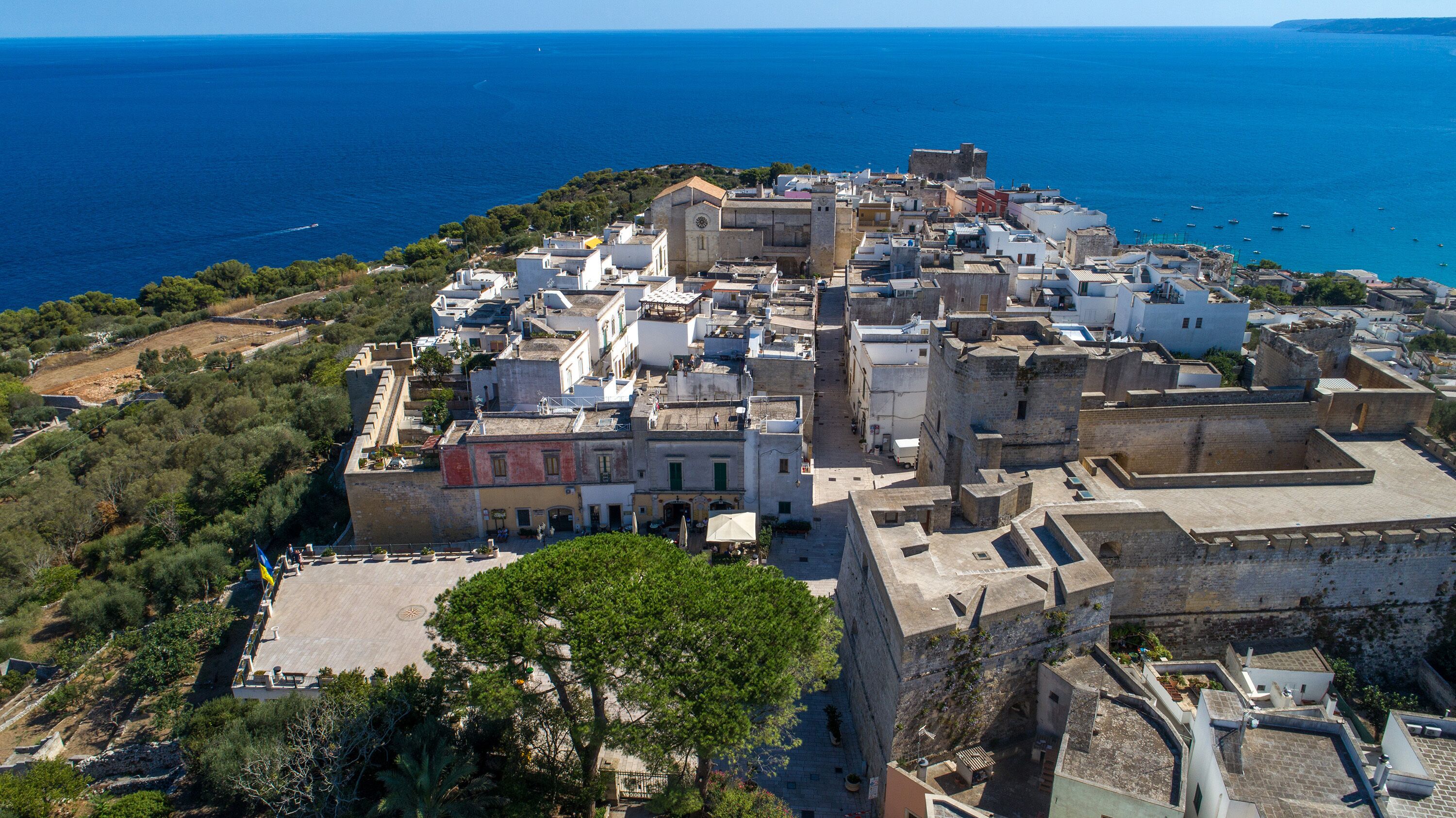 An aerial view of a coastal town with historic architecture, including a prominent castle-like structure and a church.