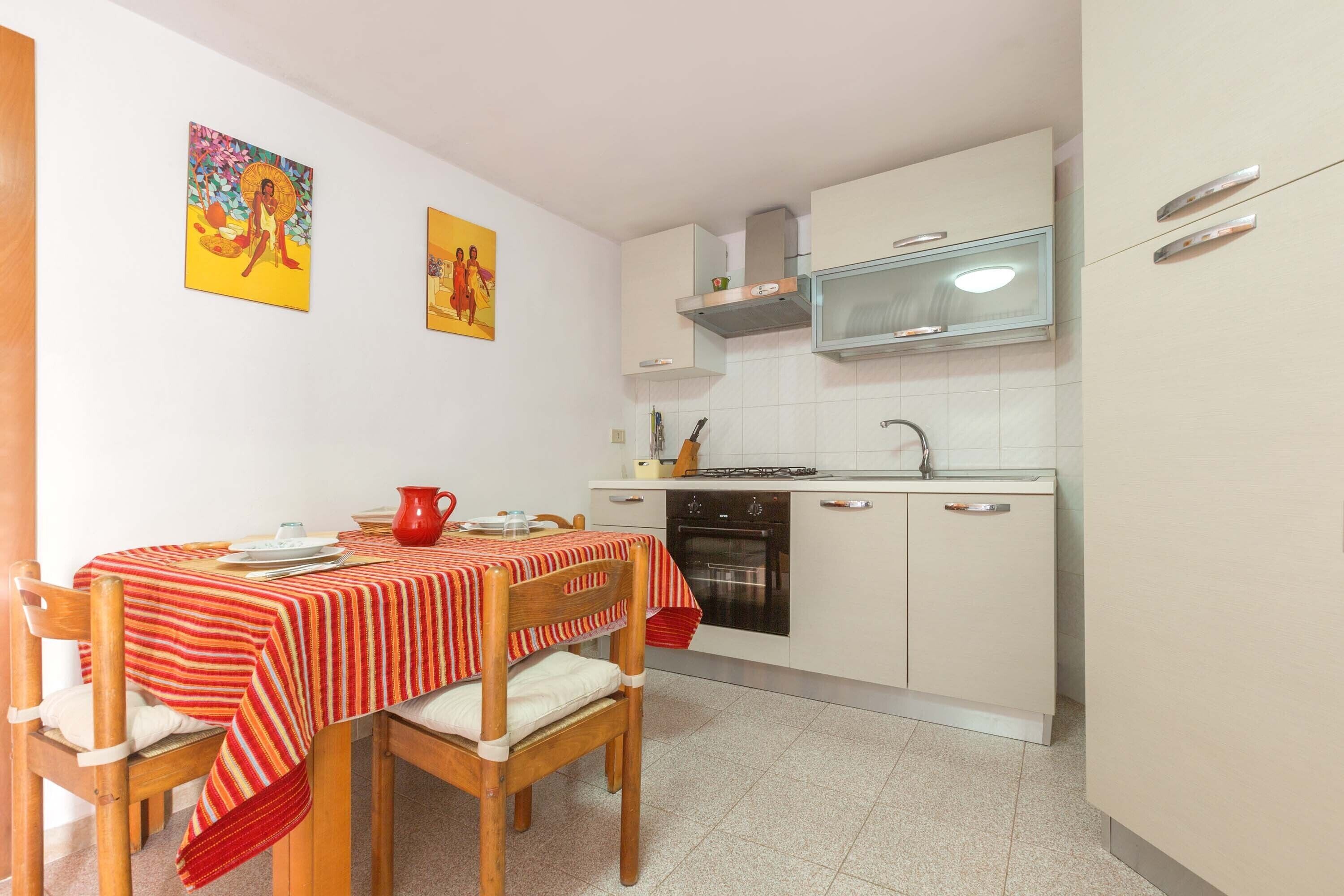 A compact kitchen with white cabinets, a microwave, and a stove. There is a dining table with a red-striped tablecloth and wooden chairs.