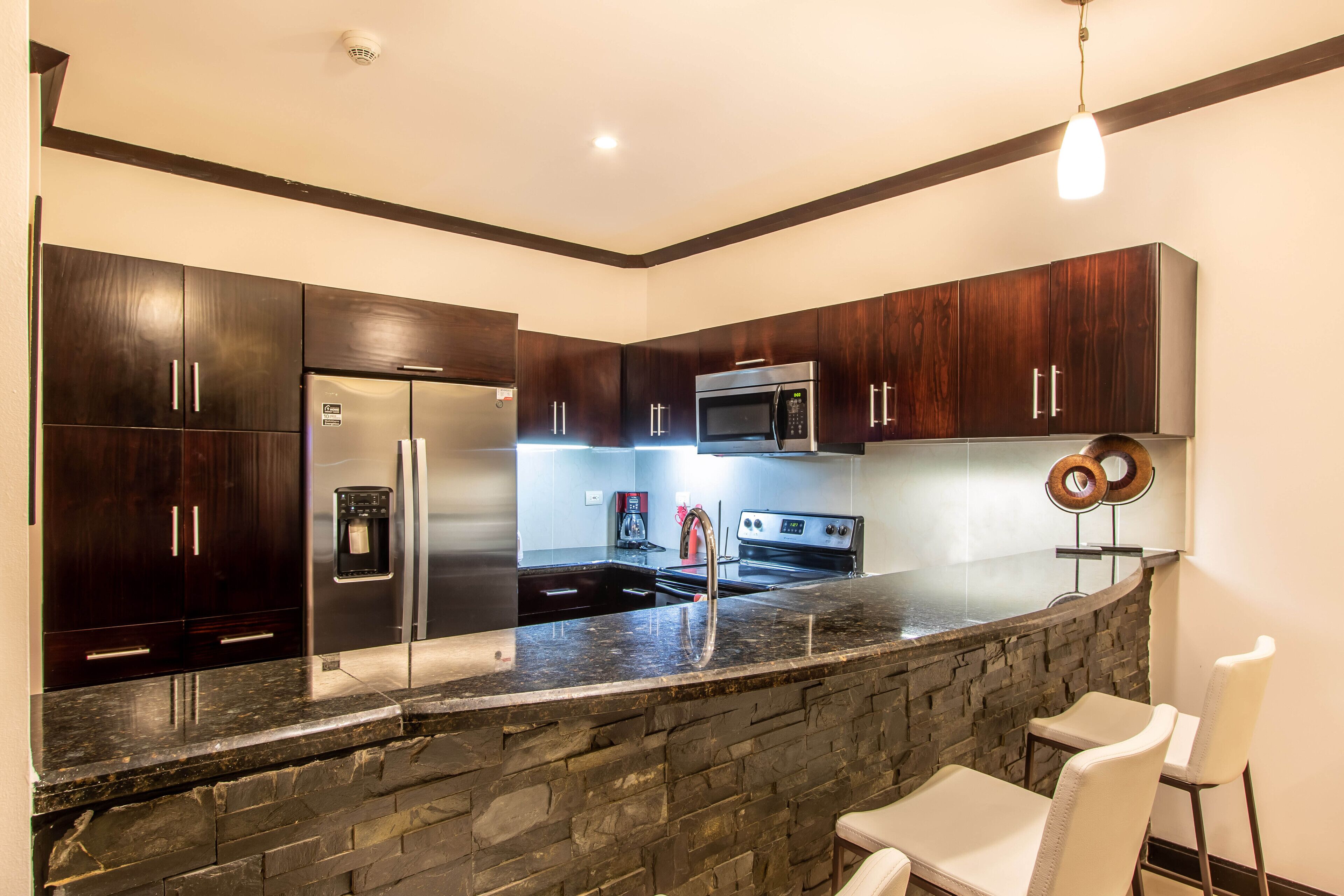 A modern kitchen with dark wood cabinets, a granite countertop, a built-in oven, and a stone accent wall.