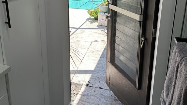 A doorway leading to a pool area with a view of a swimming pool, potted plants, and a tiled patio.