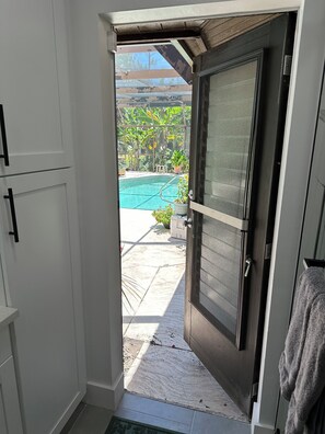 Ein Durchgang zu einem Poolbereich mit Blick auf einen Swimmingpool, Kübelpflanzen und eine geflieste Terrasse.