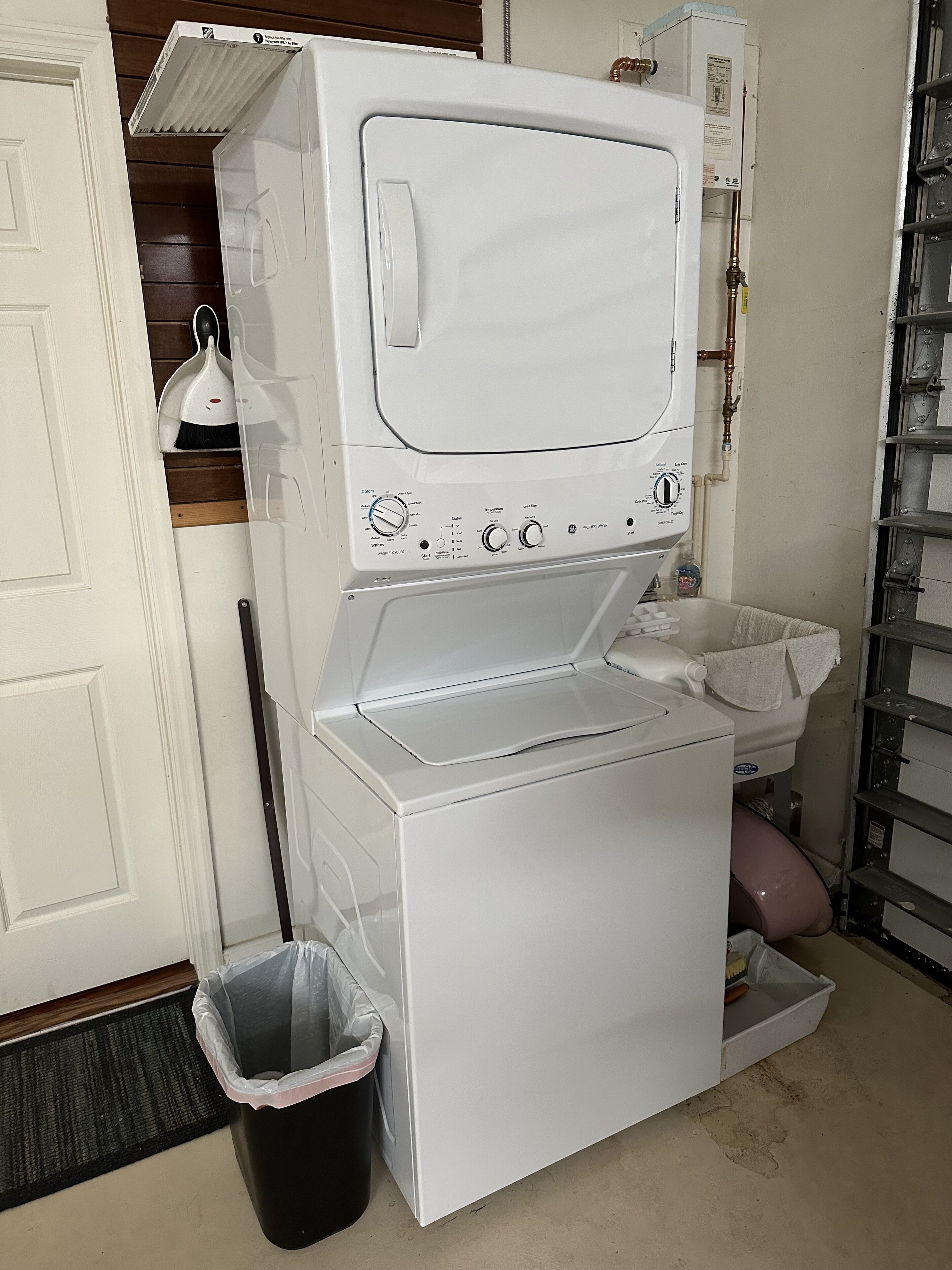 A compact, white laundry room with a washing machine and dryer, a small trash bin, and a water heater.