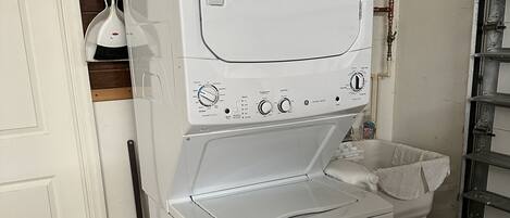 A compact, white laundry room with a washing machine and dryer, a small trash bin, and a water heater.