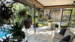 A covered patio area with a pool, seating, and various potted plants.