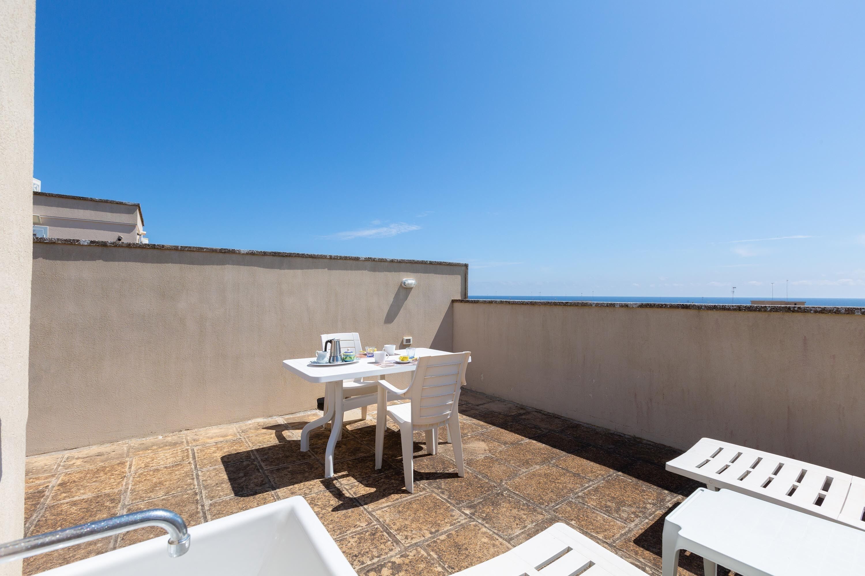 A terrace with a table and chairs, a view of the sea, and a tiled floor.