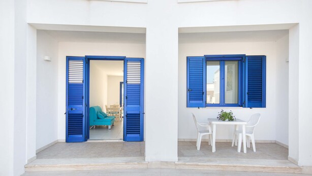 A building with two open doors leading to a room with a blue shuttered window and a table with chairs. - 3402 Casa Petrachi - PT by Barbarhouse (Melendugno)