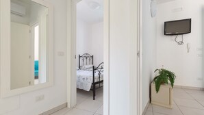 A bedroom with a bed, a bedside table with a plant, a TV mounted on the wall, and a mirror on the wall. - 3402 Casa Petrachi - PT by Barbarhouse (Melendugno)