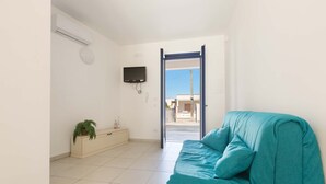 A room with a teal sofa, a small plant, a TV mounted on the wall, and a door leading outside. - 3402 Casa Petrachi - PT by Barbarhouse (Melendugno)