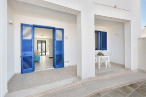 A modern building with a white exterior and blue shutters on the doors. There is a small outdoor seating area with a table and chairs.
