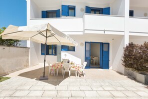 A white building with blue shutters, a patio with a table and chairs, and a large umbrella.